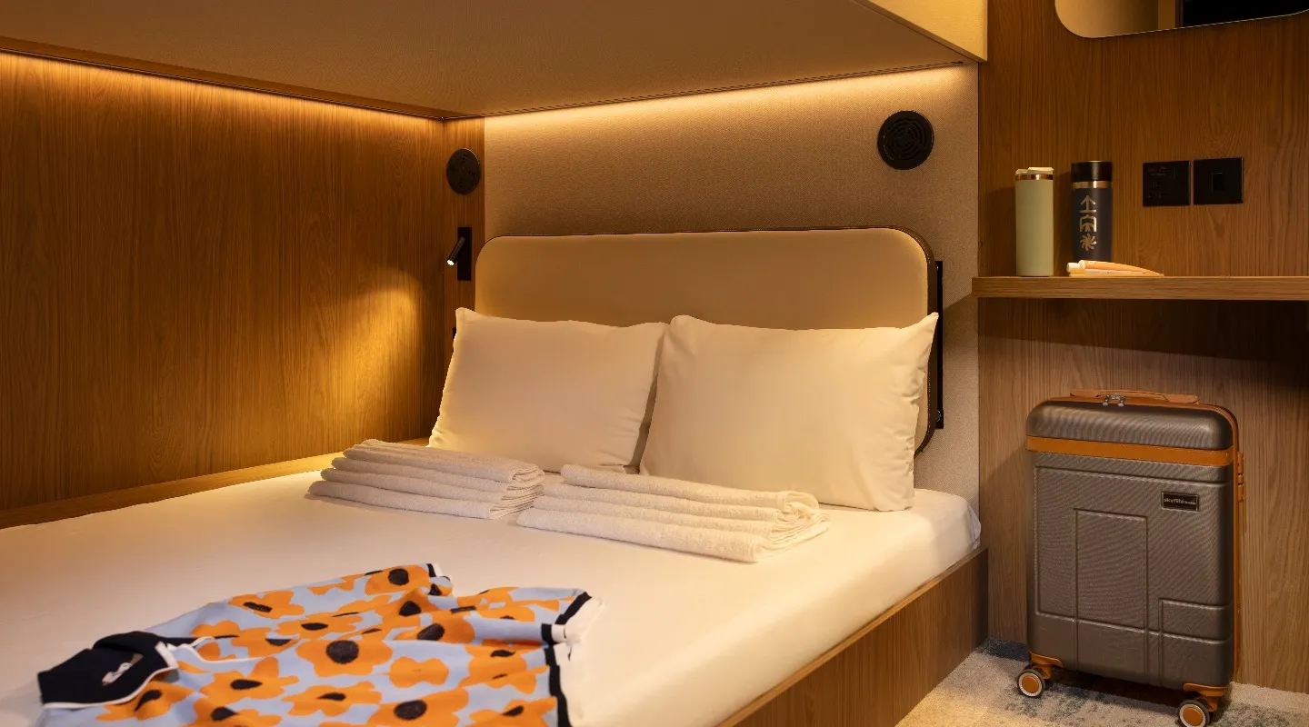 A Kabannas cabin double bed with folded towels and clothes laid out, a suitcase beside it.