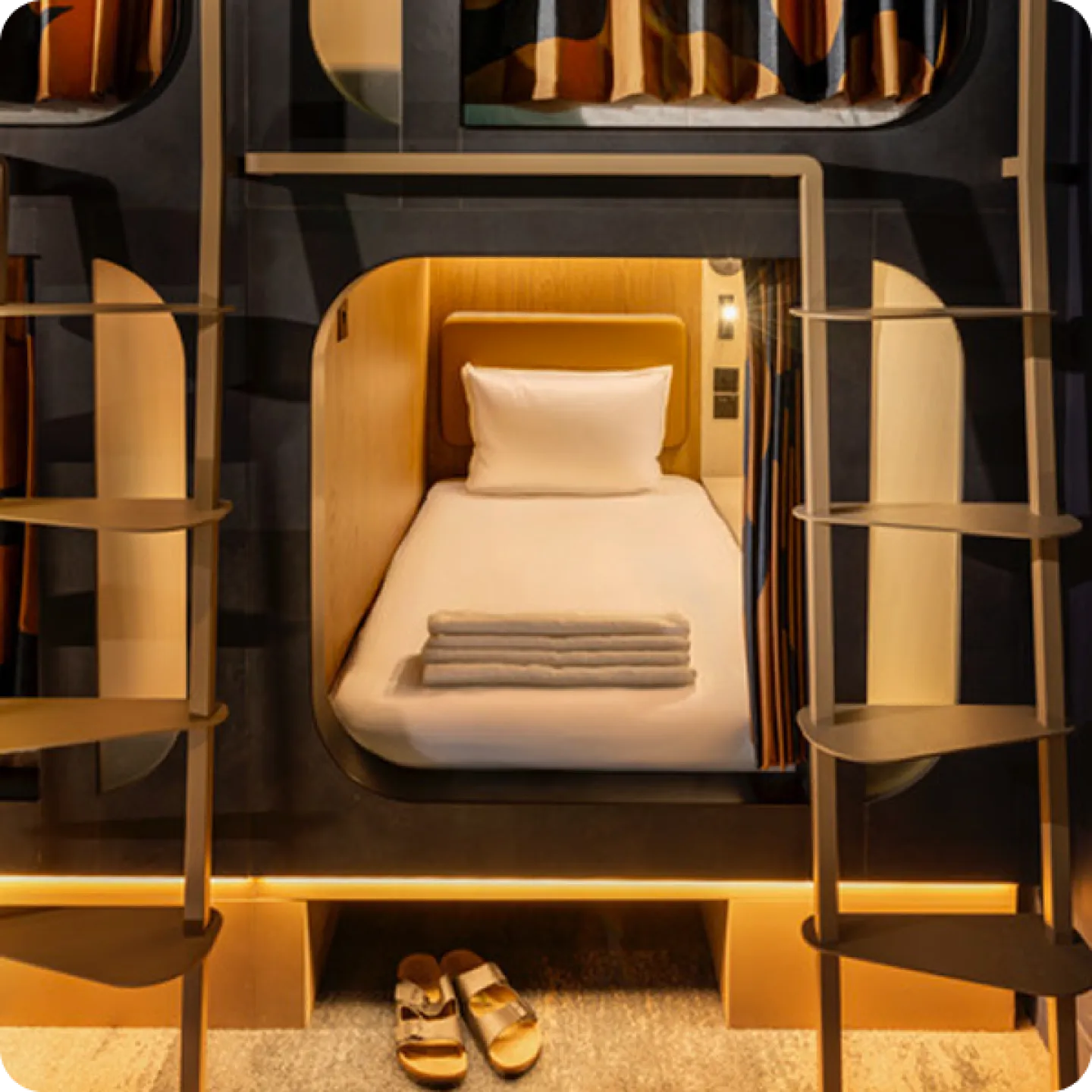 An open Kabannas pod with a made single bed and folded towels, ladders to the berths either side.