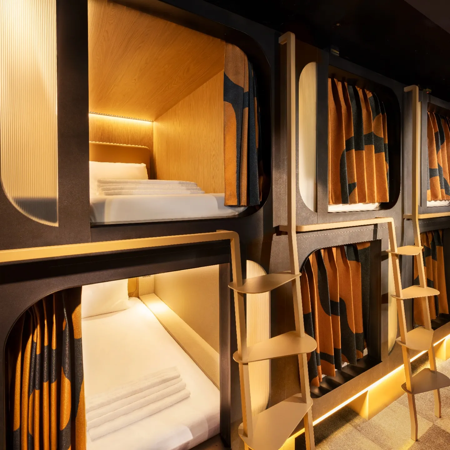 A Kabannas Pod dorm room with two levels of Pods each with a privacy curtain, clean white sheets and wood paneling 