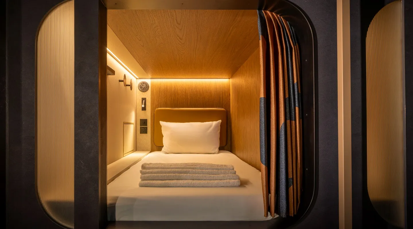 A Kabannas cabin with a single bed, folded towels, warm wood panelling and a reading light.