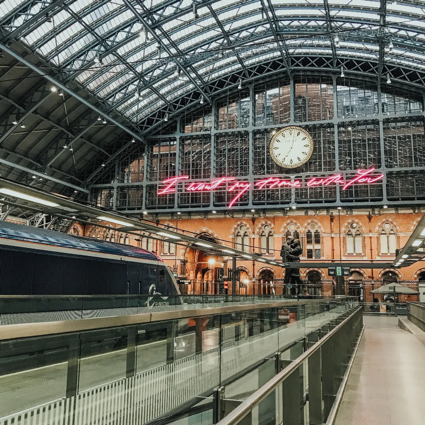 St Pancras International station: a Eurostar train beneath the glazed barrel roof, the station clock and the pink neon artwork above the platforms.